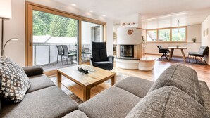A modern living room with a sofa, a coffee table, a fireplace, and a dining area with chairs. - Alpenferienwohnung in B rs (Buers)