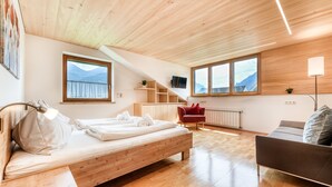 A modern room with a wooden bed, a red chair, a sofa, and large windows with mountain views. - Alpenferienwohnung in B rs (Buers)