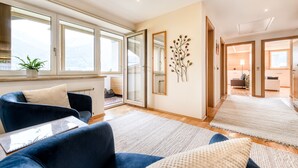 A modern living room with a sofa, a coffee table, a potted plant, and a large window. - Alpenferienwohnung in B rs (Buers)