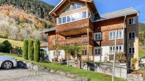 A two-story house with a balcony, surrounded by a stone wall and a driveway. - Ferienwohnung R ti - 2-zimmer mit Sw-balkon (Brand)