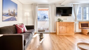 A modern living room with a sofa, a television, a wooden cabinet, and a view through a glass door. - Ferienwohnung R ti - 2-zimmer mit Sw-balkon (Brand)