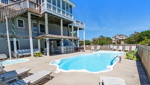 A pool area with lounge chairs, a small pool, and a two-story building with a balcony.
