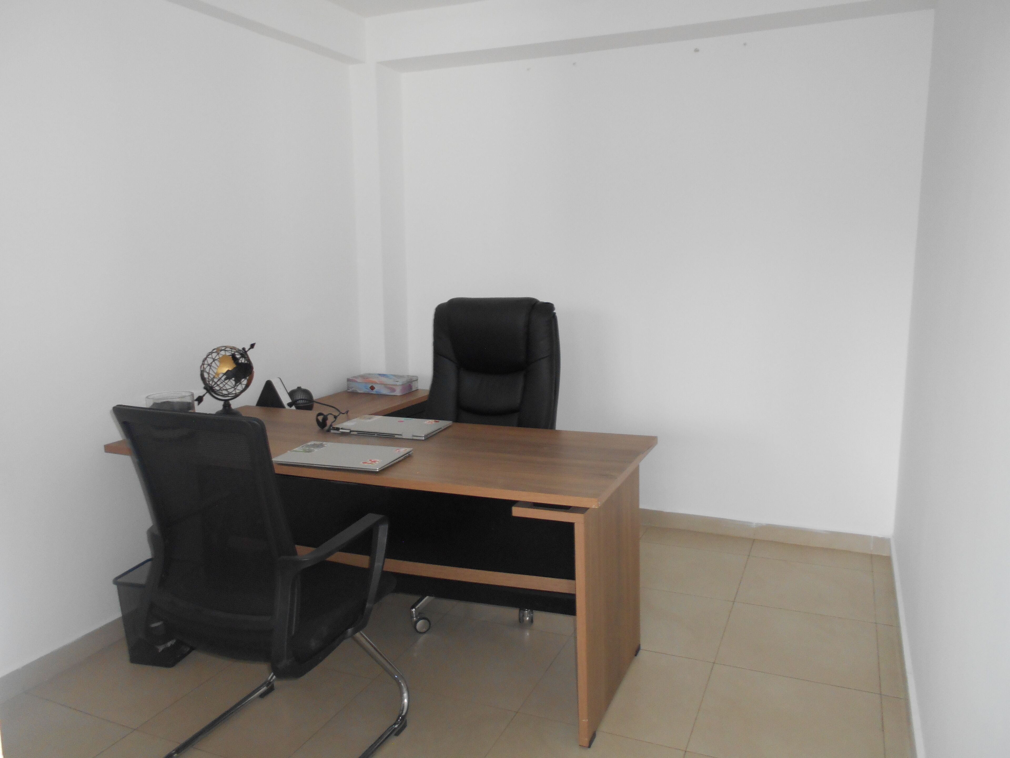 A small office space with a wooden desk, two black office chairs, a globe, and a box of tissues.
