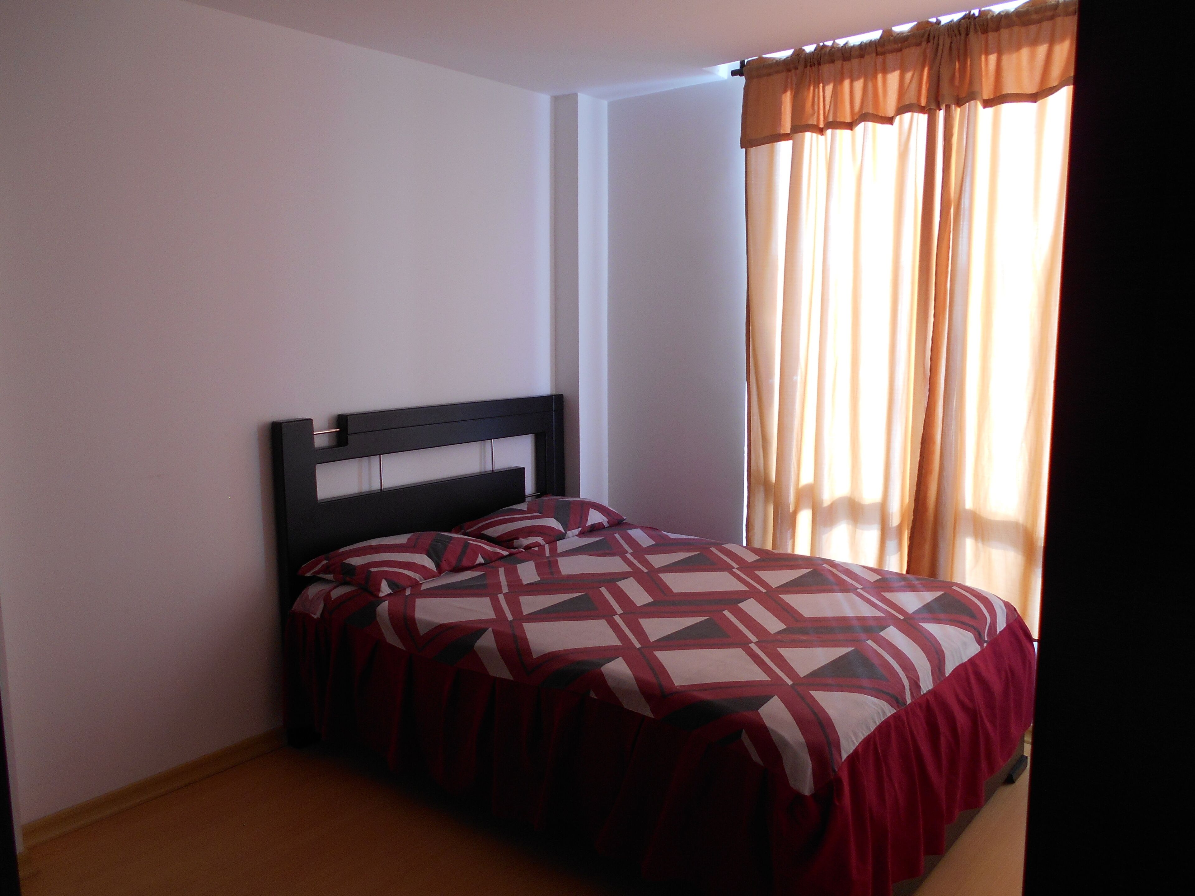 A bedroom with a bed, a headboard, and a window with curtains.