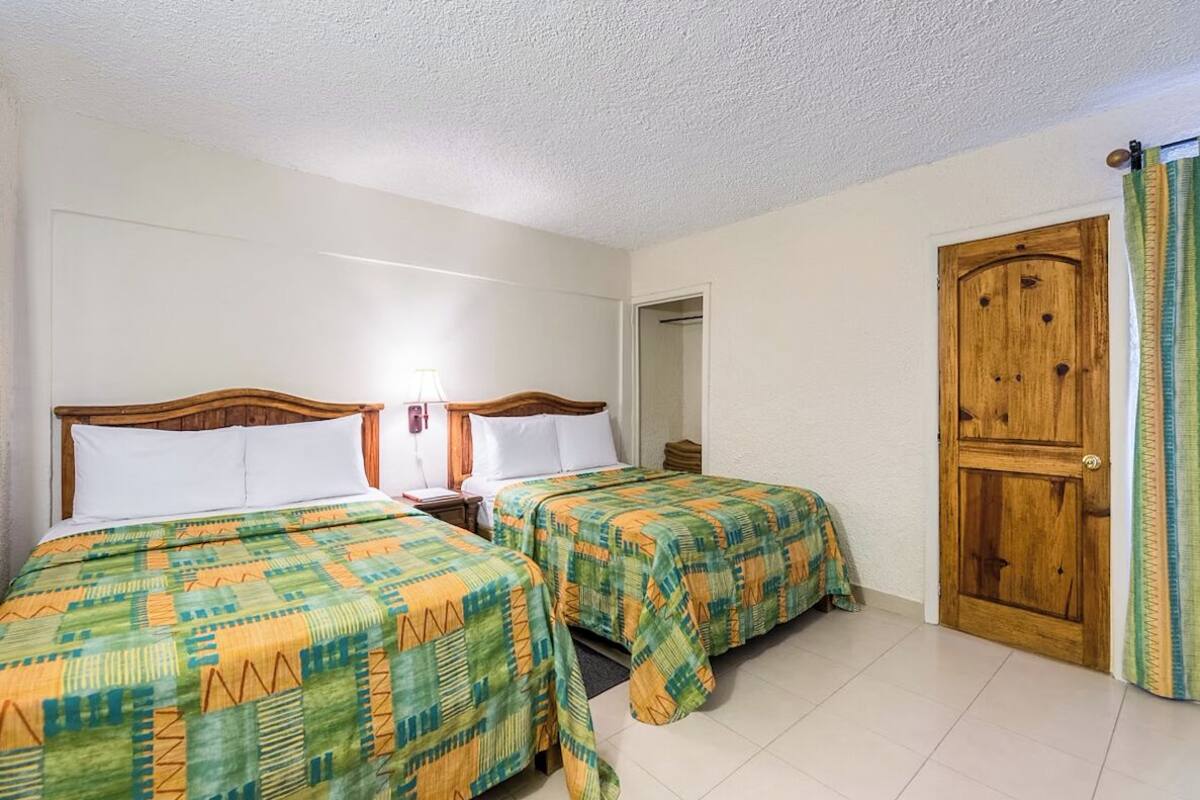 A hotel room with two beds, a wooden door, and a nightstand with a lamp.