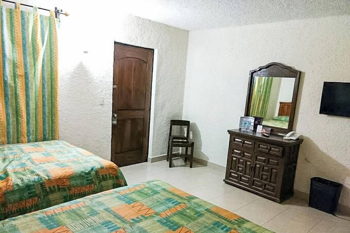 A room with two beds, a wooden dresser, a chair, a television, and a door.