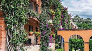 Un bâtiment à la façade en briques, doté de fenêtres en arc de cercle et d’un balcon orné de plantes en pot.