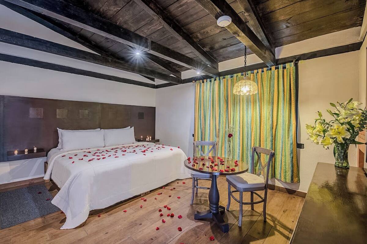 A bedroom with a bed, a table with chairs, and a vase of flowers.