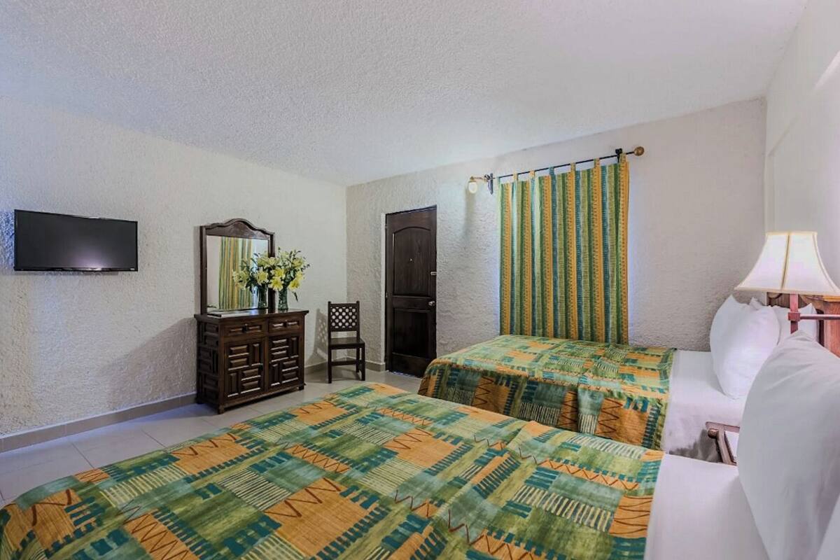 A hotel room with two beds, a TV, a dresser, a chair, and a window with curtains.