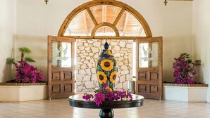 Un hall d’entrée avec un mur en pierre, des portes en bois et une table ronde agrémentée d’un vase décoratif et de fleurs.
