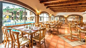 Un restaurant avec des tables et des chaises en bois, de grandes fenêtres et un sol carrelé.