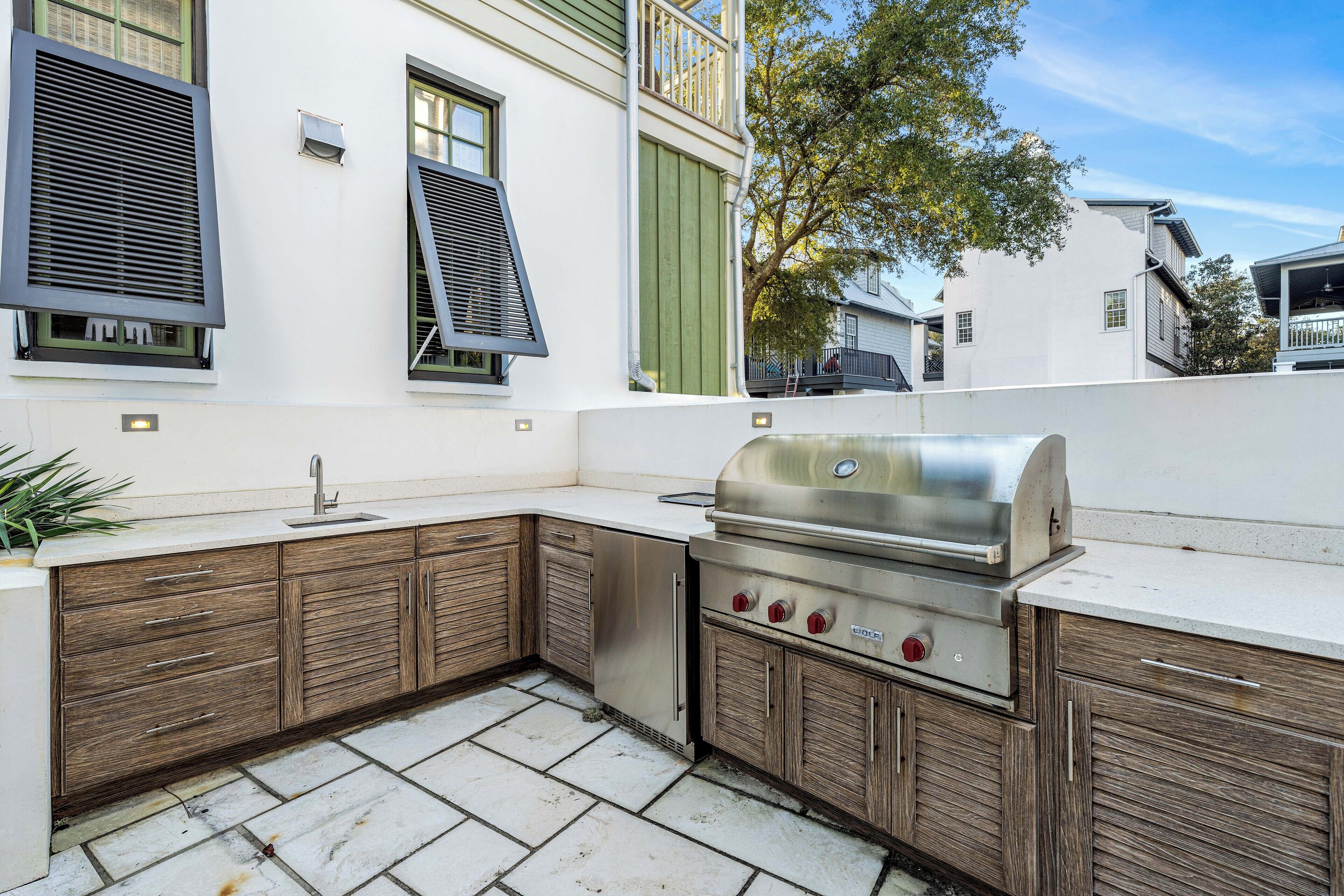 Cucina esterna con barbecue integrato, mobili in legno e pavimento in pietra.