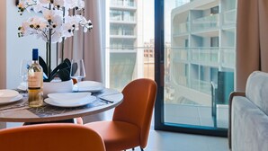 Un espace repas moderne avec une table ronde, de l’assiette blanche, une bouteille de vin et un vase rempli d’orchidées blanches.