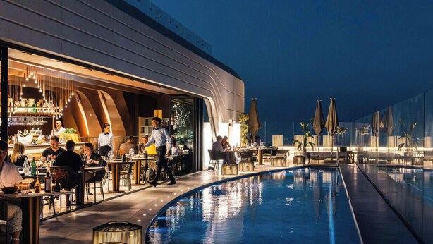 Un espace aménagé au bord de la piscine, comprenant un bar et un coin repas, ainsi qu’une piscine et une façade de bâtiment au design moderne.