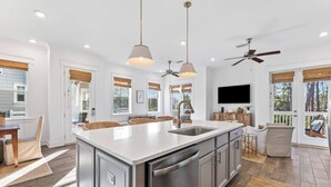 Une cuisine spacieuse dotée d’un grand îlot central, d’appareils électroménagers modernes et de luminaires suspendus.