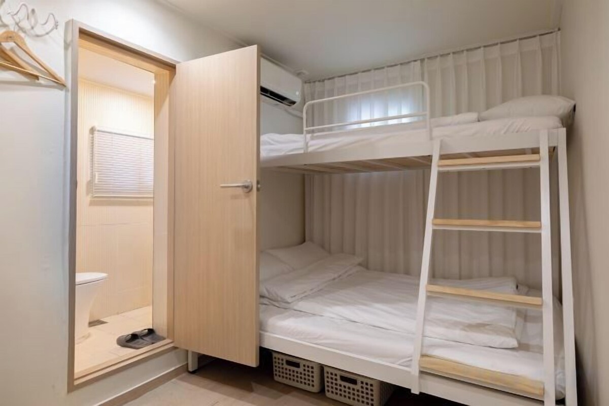A bunk bed with a wooden ladder, a white door, and a small window with blinds.