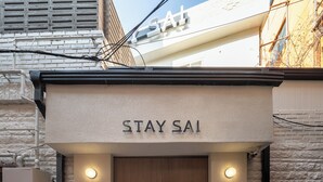 Une entrée d’immeuble avec une enseigne indiquant « STAY SAI » et une porte en bois. De chaque côté de la porte, on peut voir deux panneaux lumineux.