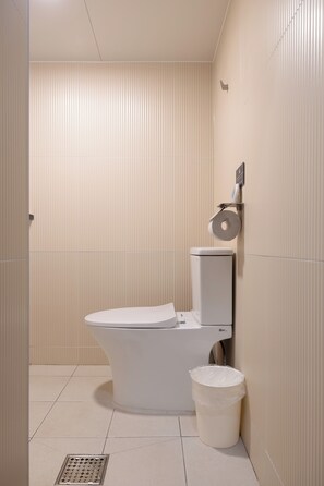 A modern bathroom with a toilet, a trash bin, and a toilet paper holder on the wall. - Stay SAI (Seoul)
