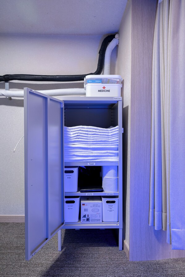 A storage unit with labeled compartments for guest items, including a medicine box, towels, toiletries, and a hair dryer.