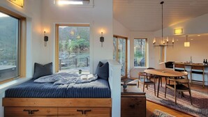A modern bedroom with a large bed, a wooden desk, and a dining area with a view of the outdoors. - Hot tub | Sauna |Firepit |Sleeps 6! (Ashland)