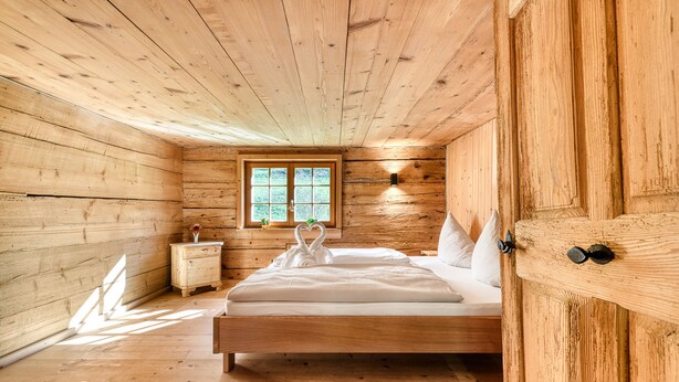A wooden cabin bedroom with a bed, nightstand, and window. - Berghaus Lutzklang in Raggal (Raggal)