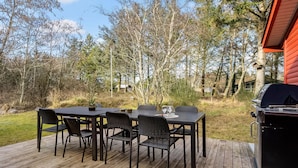 Une terrasse en bois avec une table et des chaises, entourée d’arbres et agrémentée d’un barbecue.