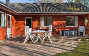 A red wooden house with a tiled roof, a brick patio, and a table with chairs.