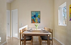 A dining room with a wooden table set for six, a vase of flowers, and a colorful abstract painting on the wall.