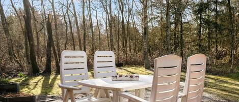 An outdoor seating area with a round table and four white chairs, surrounded by a forested landscape.
