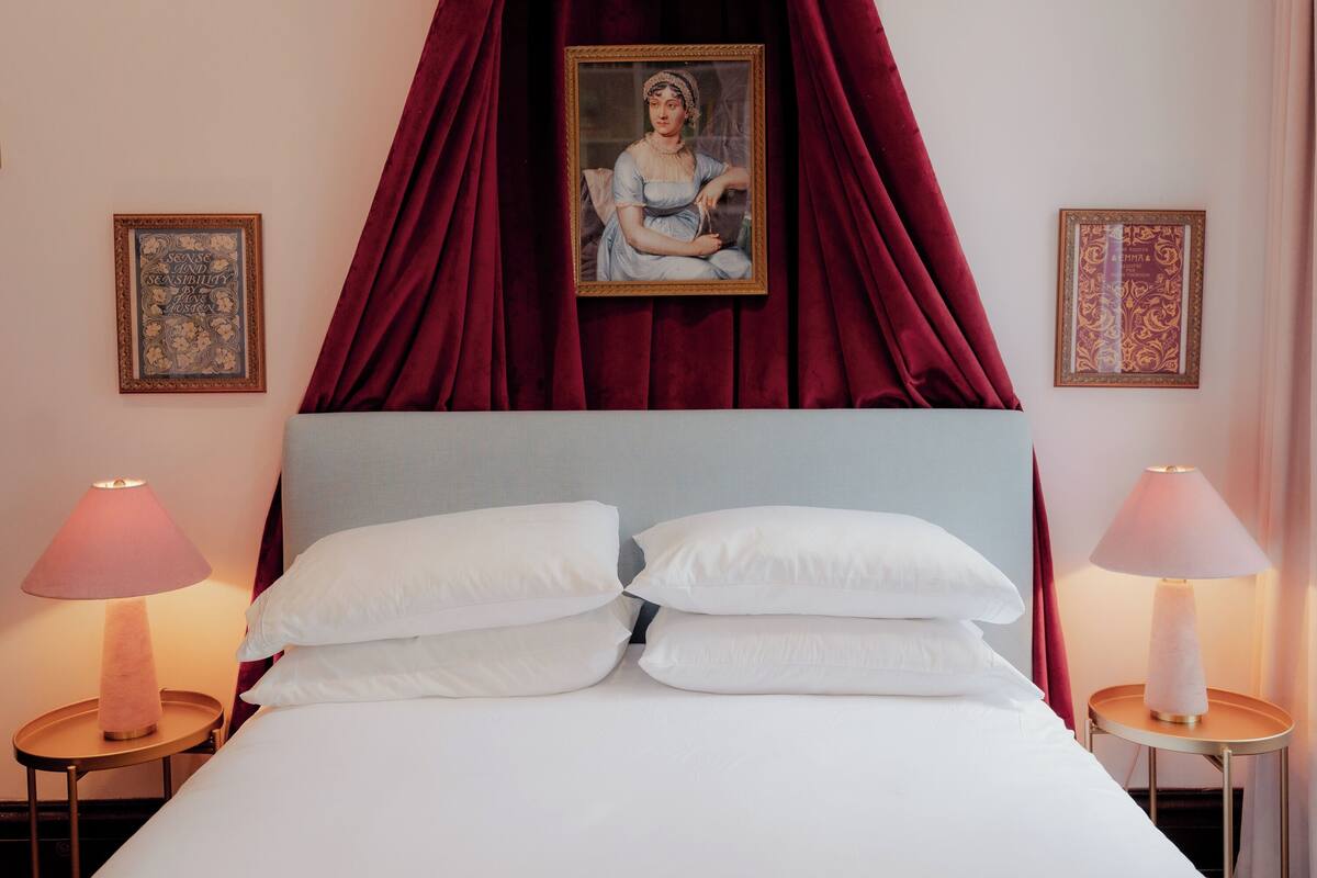 Un dormitorio con una cama, dos lámparas de noche, un dosel rojo y dos cuadros en las paredes.