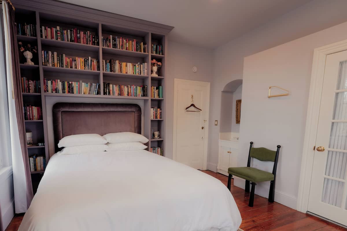 Un dormitorio con una cama grande, una estantería, una silla y una puerta.