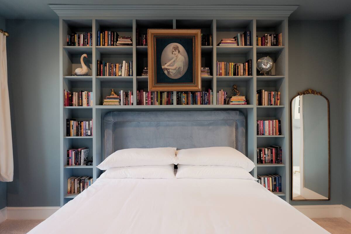 Un dormitorio con una cama grande, una estantería llena de libros, un retrato enmarcado y un espejo.