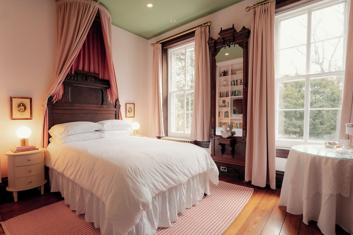 Un dormitorio con una cama grande, dos mesitas de noche con lámparas, un aparador de madera, un espejo y una ventana con cortinas.