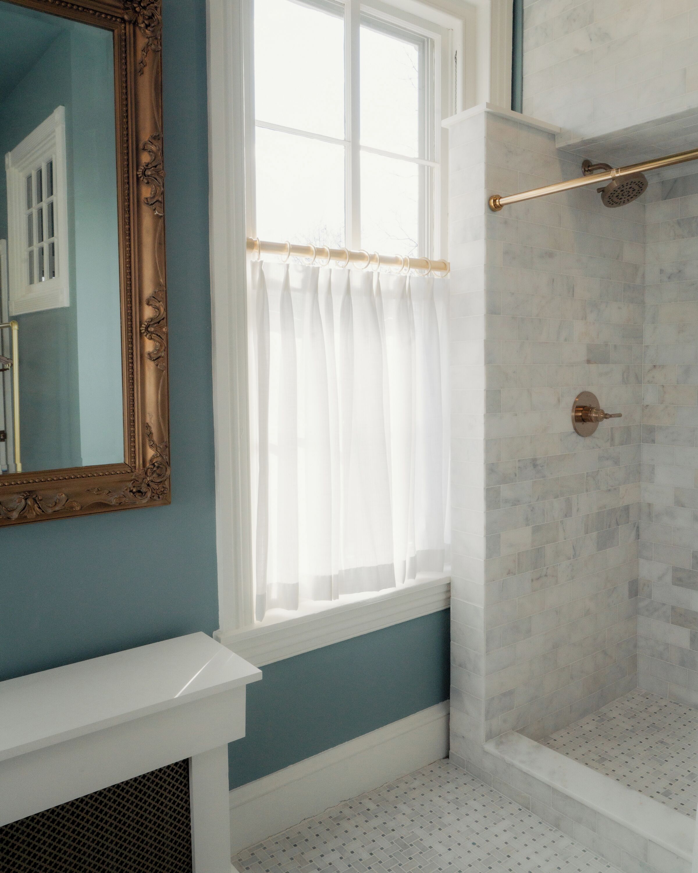Un baño con ducha, una ventana con cortinas y un espejo con marco decorativo.