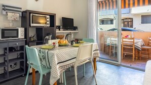 A compact kitchen with a microwave, toaster, and coffee maker. A dining table with chairs is set up near a sliding glass door leading to an outdoor area.
