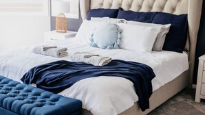A neatly made bed with white and blue bedding, a blue throw blanket, and a matching blue bench. - Riverside Retreat Pool, Pontoon & Space (Bundall)