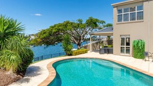 A swimming pool with a curved edge, a covered patio area, and a view of the sea. - Riverside Retreat Pool, Pontoon & Space (Bundall)