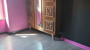 A room with a large wooden wardrobe against a purple wall, a wooden floor, and a pink rug. - Country house near spa  (Vandenesse)