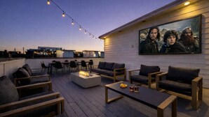 A rooftop terrace with outdoor seating, a fire pit, and a large movie poster on the wall. - Songbird Suites - 2 Rooftops & Outdoor Cinema (Nashville)