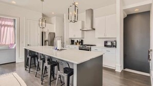 A modern kitchen with a central island, bar stools, stainless steel appliances, and pendant lighting. - Songbird Suites - 2 Rooftops & Outdoor Cinema (Nashville)