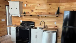 A compact kitchen with wooden walls, a stove, sink, and a refrigerator. - Charming 2-bedroom cabin with WiFi, AC 5 minutes away from Lake Guntersville (Guntersville)