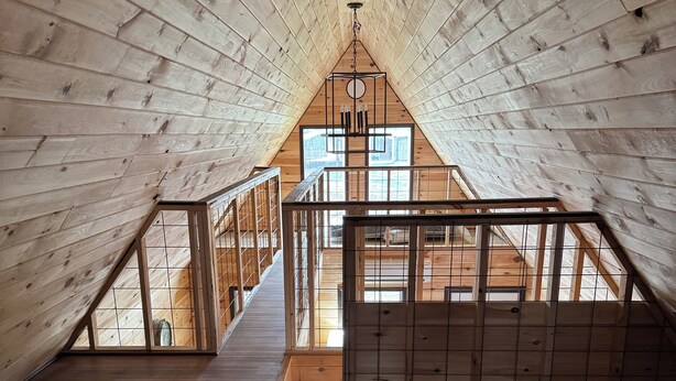 A high-ceilinged attic bedroom with wooden walls and floors, a skylight, and a view of the outdoors. - Charming 2-bedroom cabin with WiFi, AC 5 minutes away from Lake Guntersville (Guntersville)