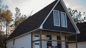 A single-story building with a gabled roof, a covered porch with two chairs, and a small staircase leading to the entrance. - Charming 2-bedroom cabin with WiFi, AC 5 minutes away from Lake Guntersville (Guntersville)