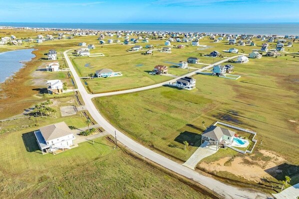 An aerial view of a coastal residential area with houses, a road, and a beach.