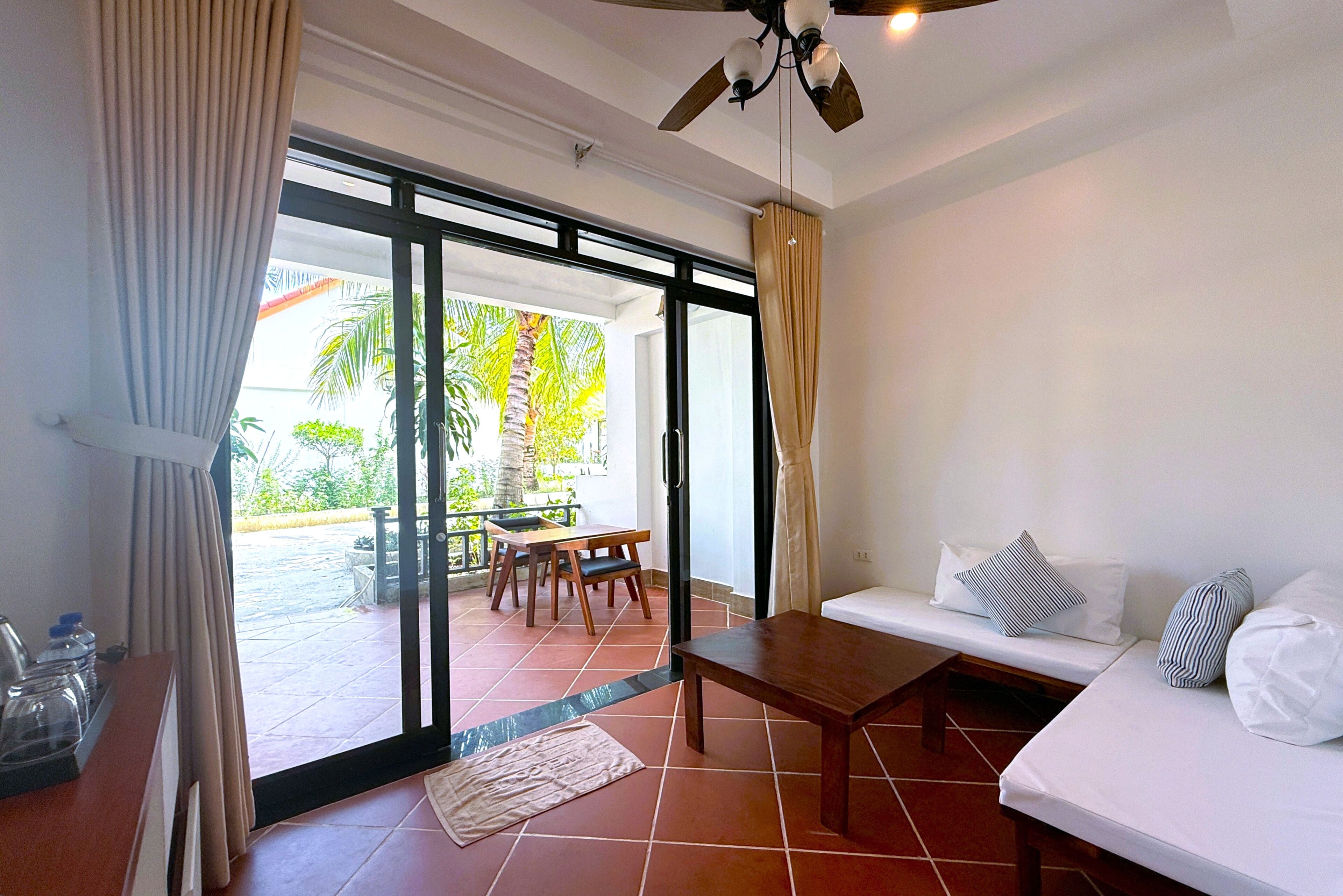 Habitación con puerta de vidrio corredera que da a un espacio exterior, una mesa de madera, un sofá con cojines y un ventilador de techo.