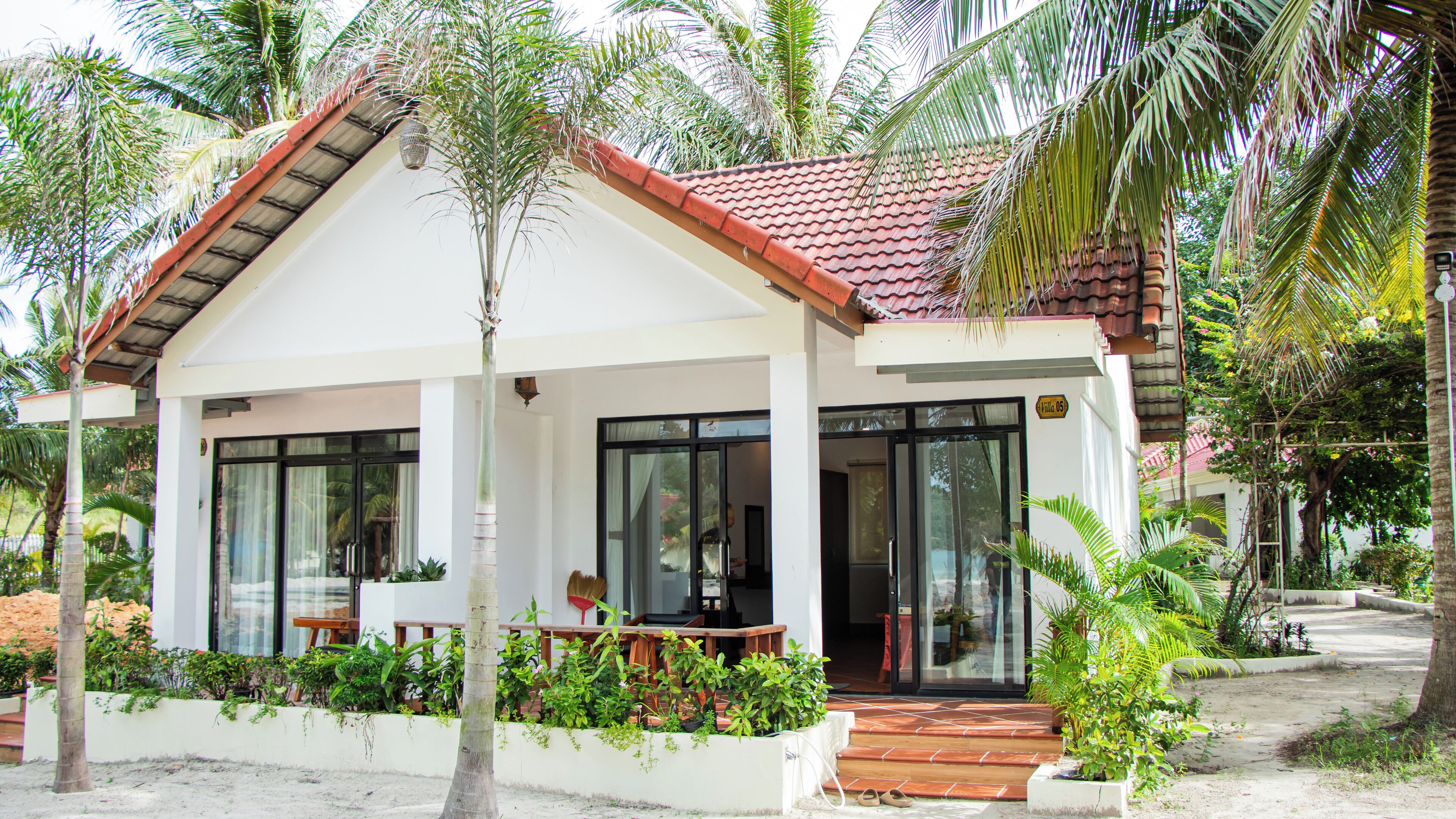 A two-story building with a red-tiled roof, large windows, and a covered porch with plants.
