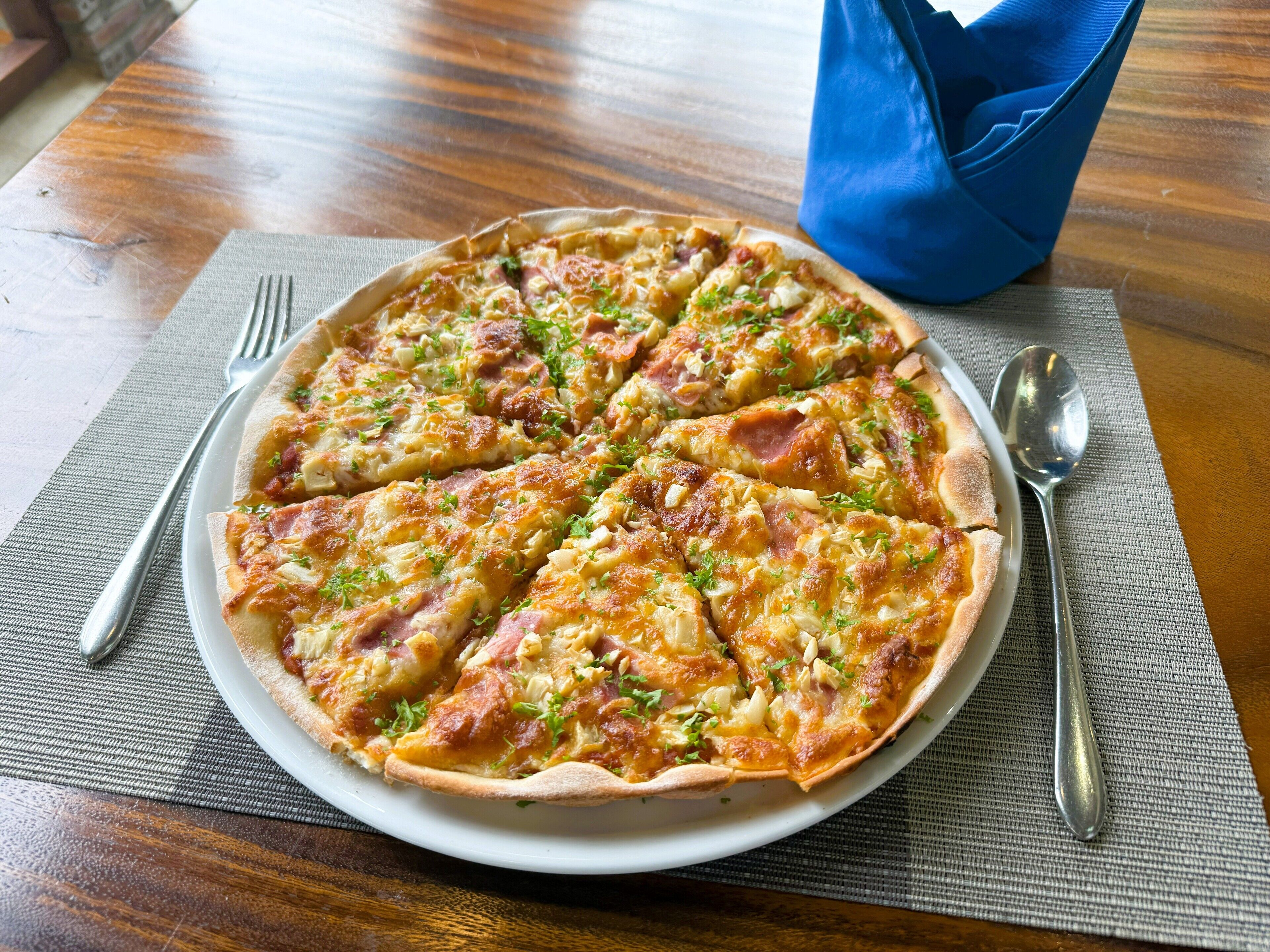 A pizza on a white plate with a fork and spoon on a placemat.