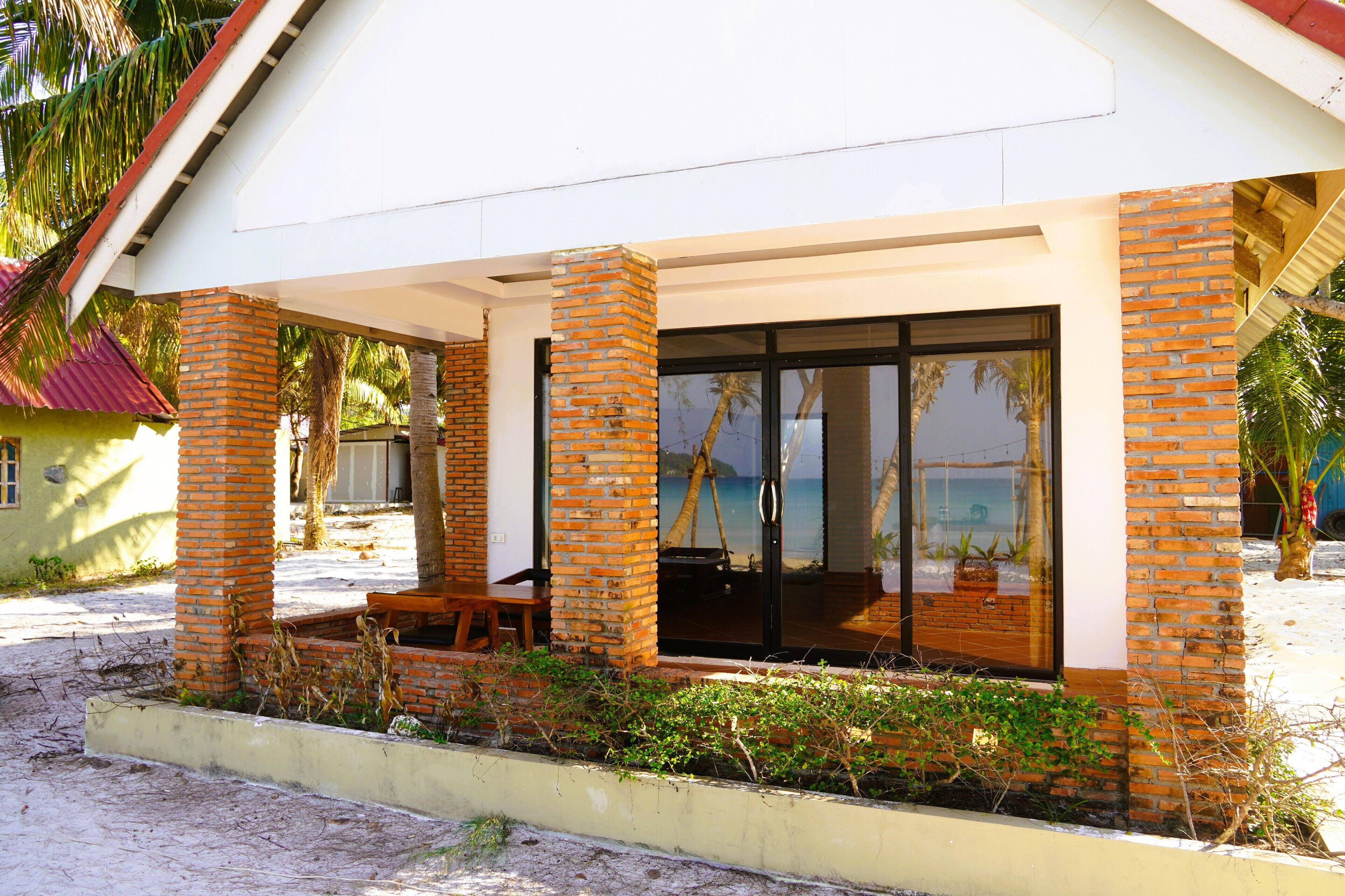 A beachfront property with a covered patio, large glass windows, and a view of the sea.