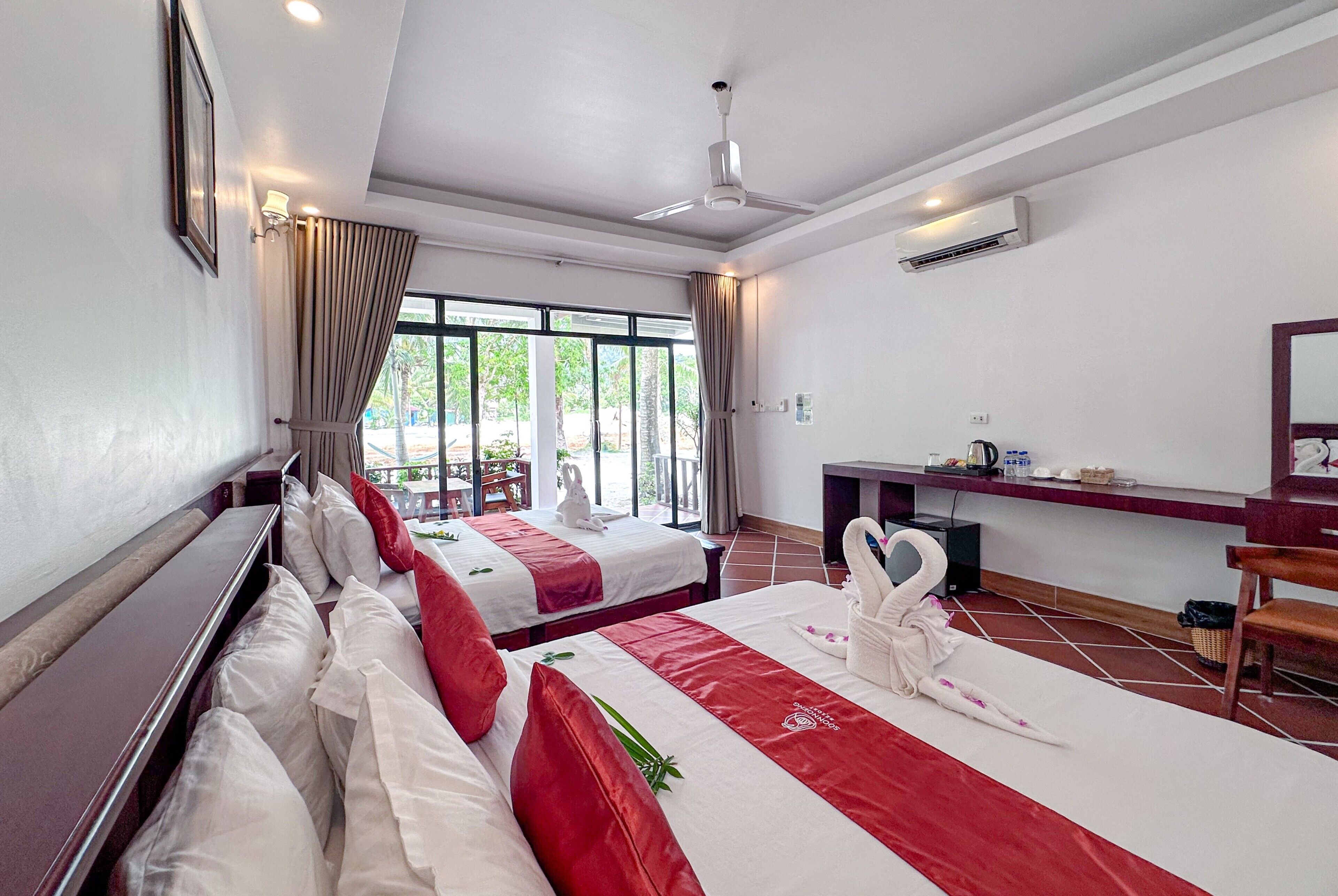 A hotel room with two beds, a desk, a chair, a ceiling fan, and an air conditioning unit.