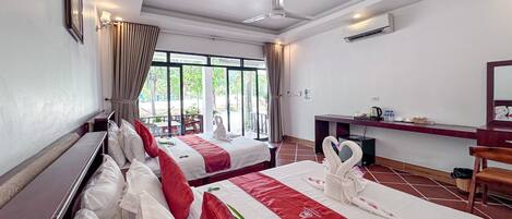 A hotel room with two beds, a desk, a chair, a ceiling fan, and an air conditioning unit.